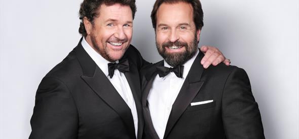 Two men in black and white suits on a plain background