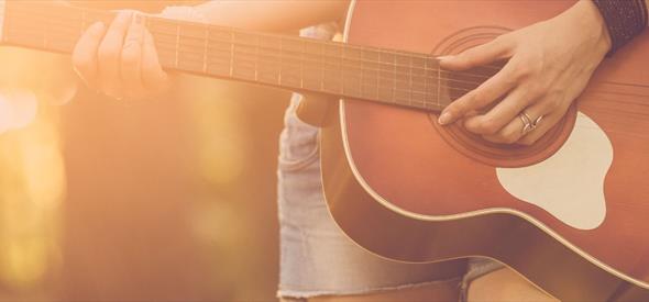 Close up of musician playing an acoustic guitar outdoors in the sunshine