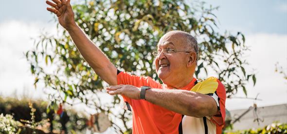 Man with bright colour block shirt smiling and holding hands in the air
