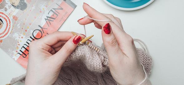 Hands knitting with tea and magazine beside her
