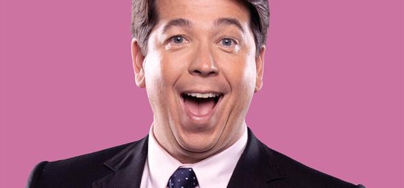 Image of man smiling with a pink background behind him.