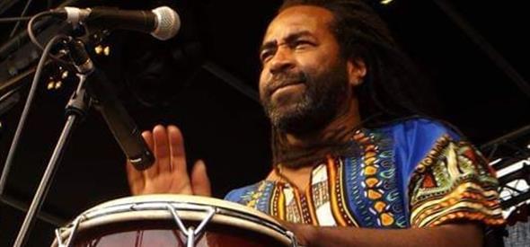 Caribbean man playing the conga drums in front of a microphone wearing traditional costume