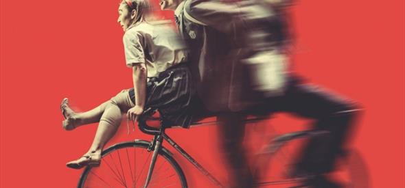 Three people on one bike against a red background