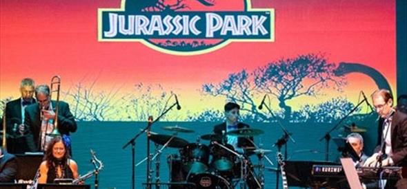 Orchestral band playing in a spotlight in front of a movie themed poster.