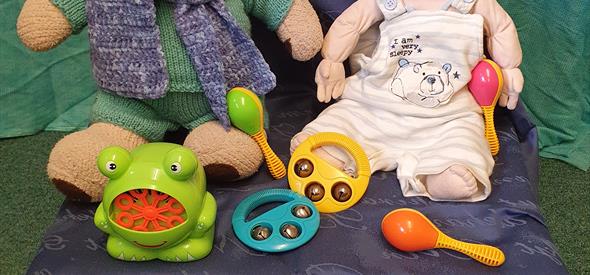 A teddy and a doll surrounded by children's rattles and toys