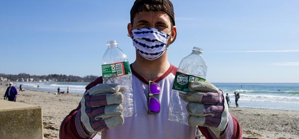 Photo of man holding two plastic bottles on beach, during beach litter pick
