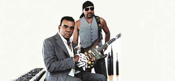 two men in suits facing camera and playing guitar