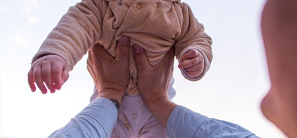 A smiling baby being hoisted lovingly in the air.