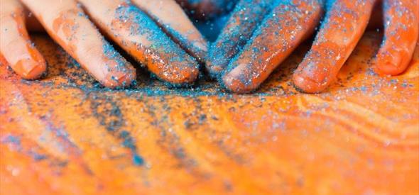 A child's hands covered in blue glitter on a wooden table.