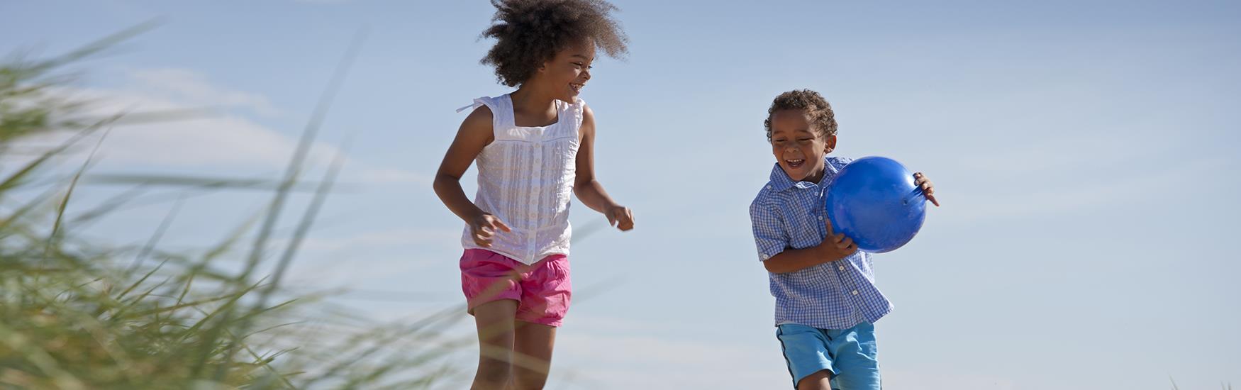 Two kids running around the beach with a ball on a sunny day in Christchurch