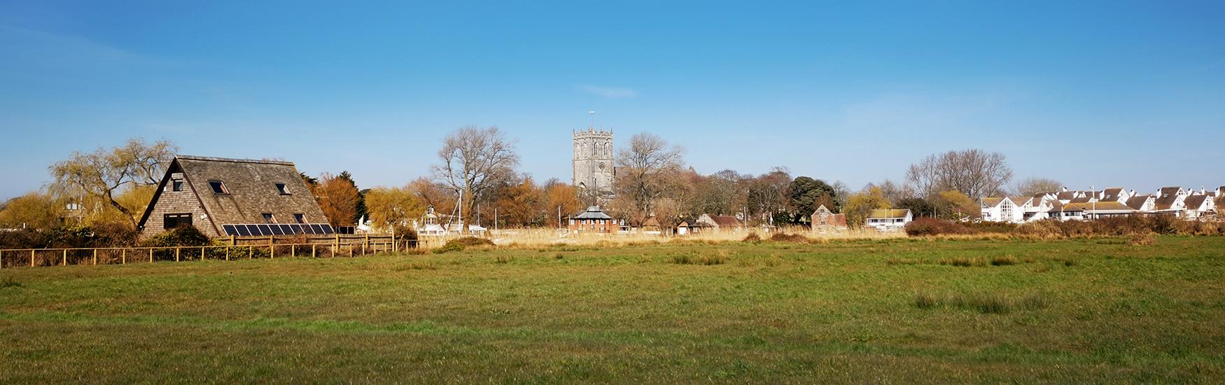 Lush green grassy field with a Barn in it with Christchurch priory peeking out behind the trees