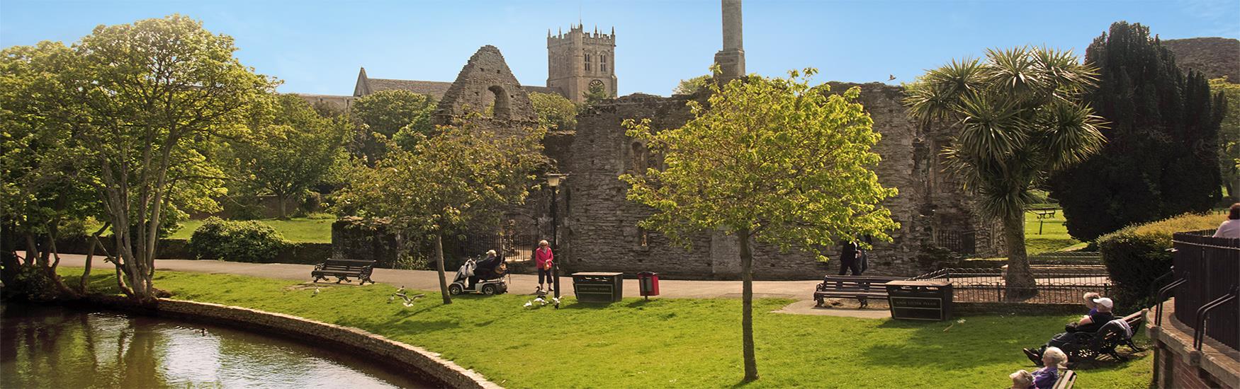 Ruins lay behind people sunbathing and sitting in the Gardens located in the town