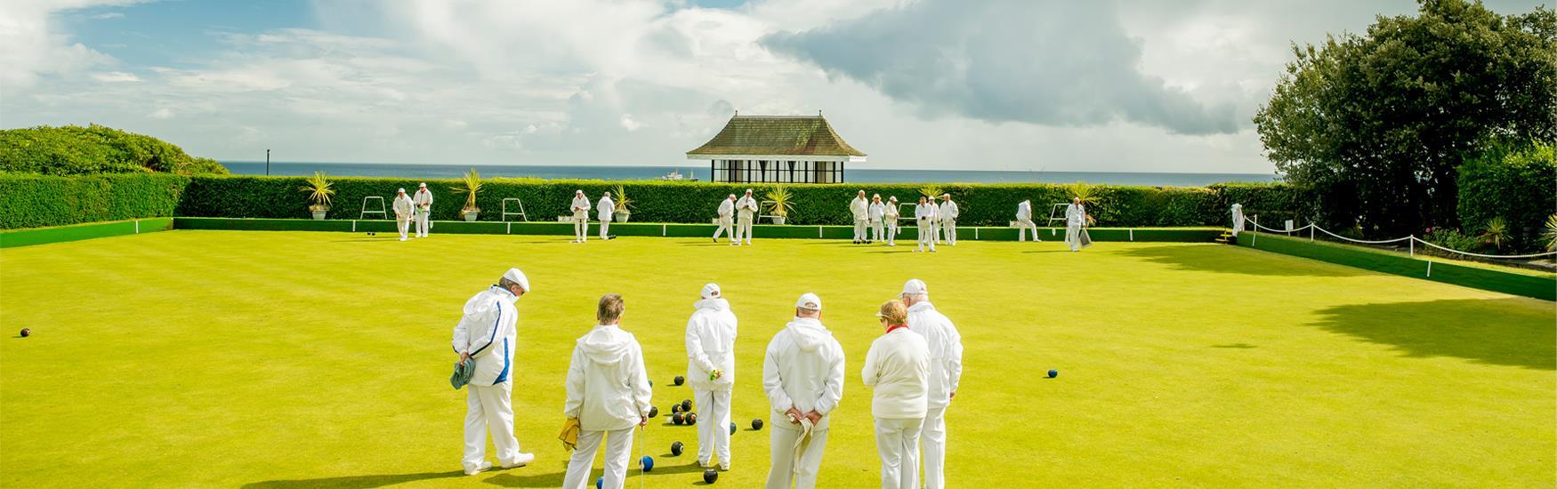 Group of people playing bowls on lush green grass with a stunning view of the sea