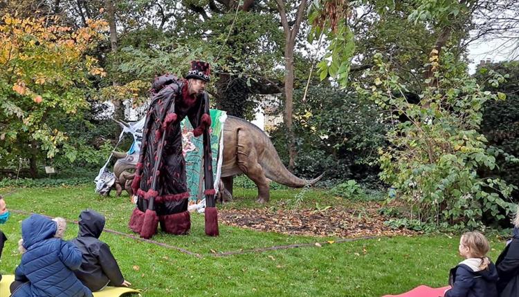 Children sat on the grass in a garden with Spidery Ben telling a spooky story.