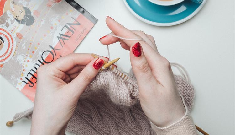 Hands knitting with tea and magazine beside her