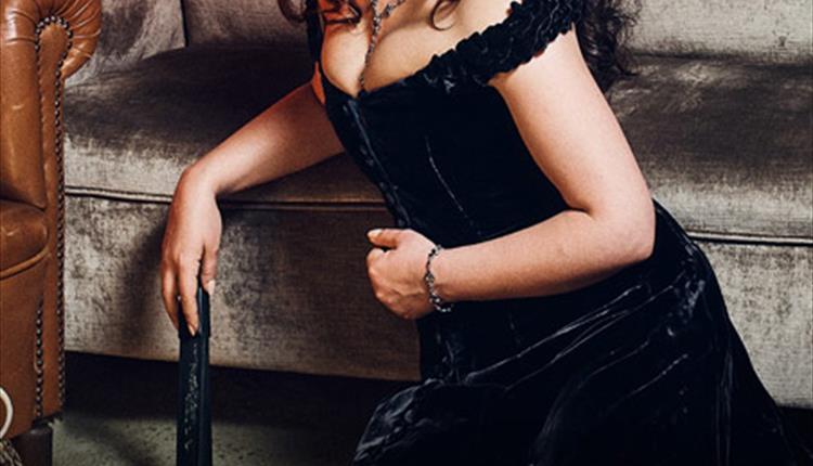 Woman sitting down and leaning on a velvet sofa with  an evening dress on