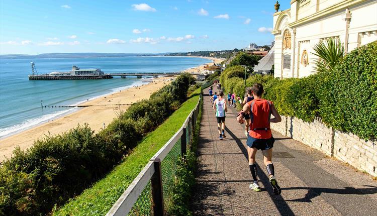 People running down cliff top towards pier with a blue sky