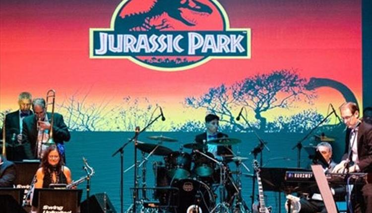 Orchestral band playing in a spotlight in front of a movie themed poster.