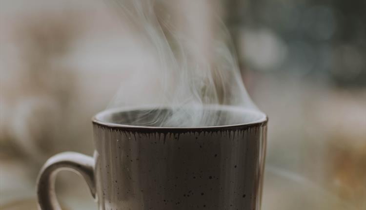 A mug containing a hot drink resting on an open book.