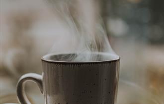 A mug containing a hot drink resting on an open book.