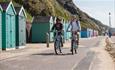 Couple cycling along Bournemouth seafront with beach huts behind them