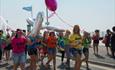 Group of people walking with the parade holding balloons and dressed up in bright amazing colours for Bourne pride