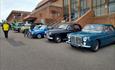 Blue, black and turquoise classic cars in a row with the BIC in the background.