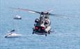 Chinook flying over the sea with boats moored up watching