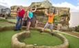 Mixed emotions as child celebrates putts the golf ball and father puts his heads in his hands