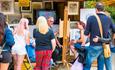 Artist creating caricature of woman whilst showing casing his artwork behind them