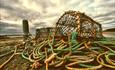 A salty and sea-worn image of cray fish catching ropes and cages with a moody cloud-scape in the background